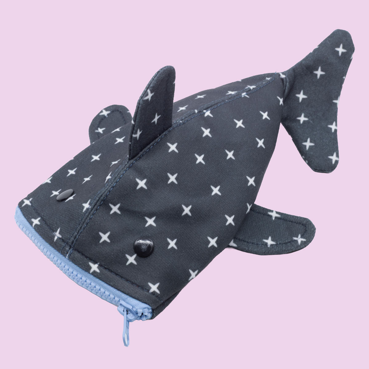 The Shark Week Pouch is a cute whale shark-shaped pouch with a gray body, white X patterns, light blue zipper as its mouth, and black button eyes—perfect for period products. Styled on a pale pink background.