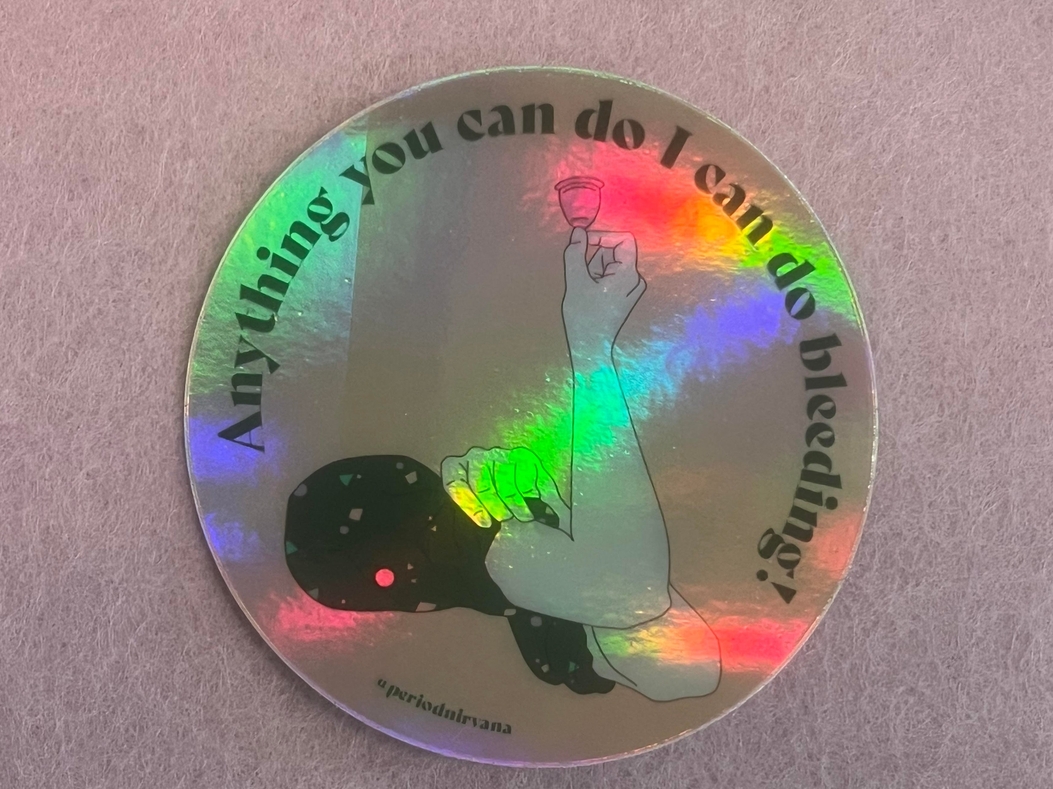 The Rosie Sticker is a round, water-resistant holographic vinyl sticker featuring a raised hand with a menstrual cup and the text "Anything you can do I can do bleeding!" with #perioddrama at the bottom.