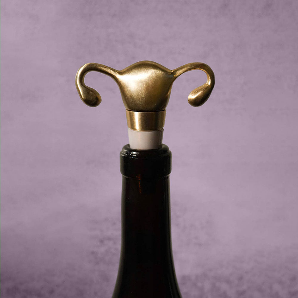 A Uterus Wine Stopper shaped like a uterus and fallopian tubes tops a wine bottle, making a unique reproductive health gift, displayed on a neutral gray background.