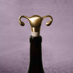 A Uterus Wine Stopper shaped like a uterus and fallopian tubes tops a wine bottle, making a unique reproductive health gift, displayed on a neutral gray background.