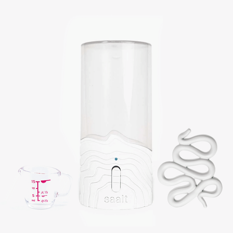 The Saalt Cup + Disc Steamer and Accessories Bundle includes a clear cylindrical device with a white base, a glass measuring cup with pink markings, and a white Spot Drying Rack—ideal for sanitizing period products.