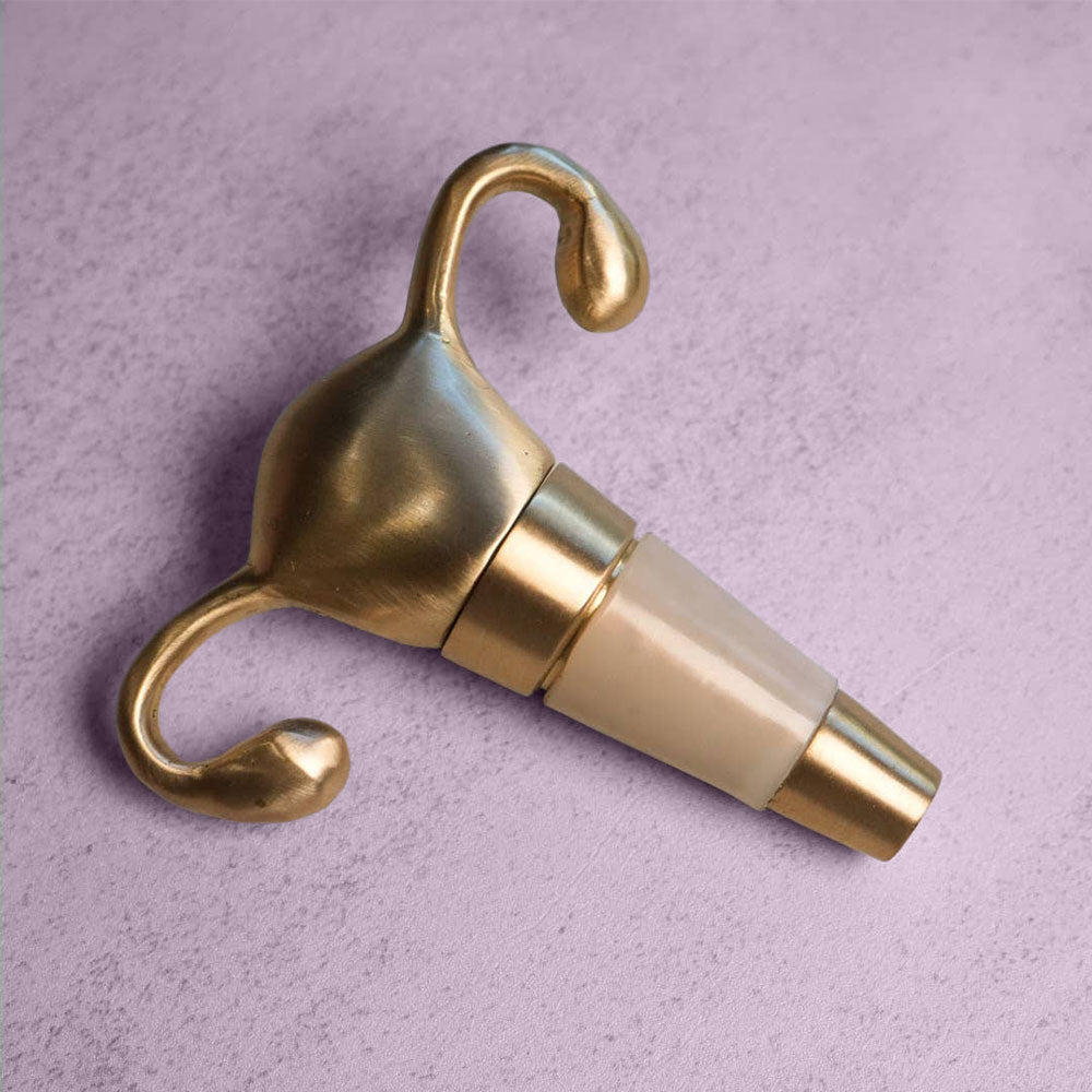The Uterus Wine Stopper, featuring a gold-colored design, rests on a light gray textured surface—an ideal reproductive health-themed gift.