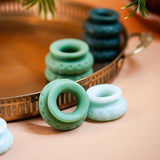 A set of four blue and green Ohnut Buffer Rings, designed for penetration depth control, are displayed on a peach surface beside a decorative metal tray; some rings rest on the tray while others are arranged in front.