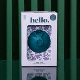 A teal Hello Disc menstrual disc sits on a reflective surface with a green striped background. Its decorative box displays floral designs and highlights leak-proof period protection and a one-size fit.