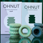 Two boxes labeled Ohnut Buffer Rings - Set of 4 stand behind soft, stretchy, body-safe rings in green and blue, designed for comfortable penetration depth control for curious couples.