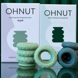 Two boxes labeled Ohnut Buffer Rings - Set of 4 stand behind soft, stretchy, body-safe rings in green and blue, designed for comfortable penetration depth control for curious couples.