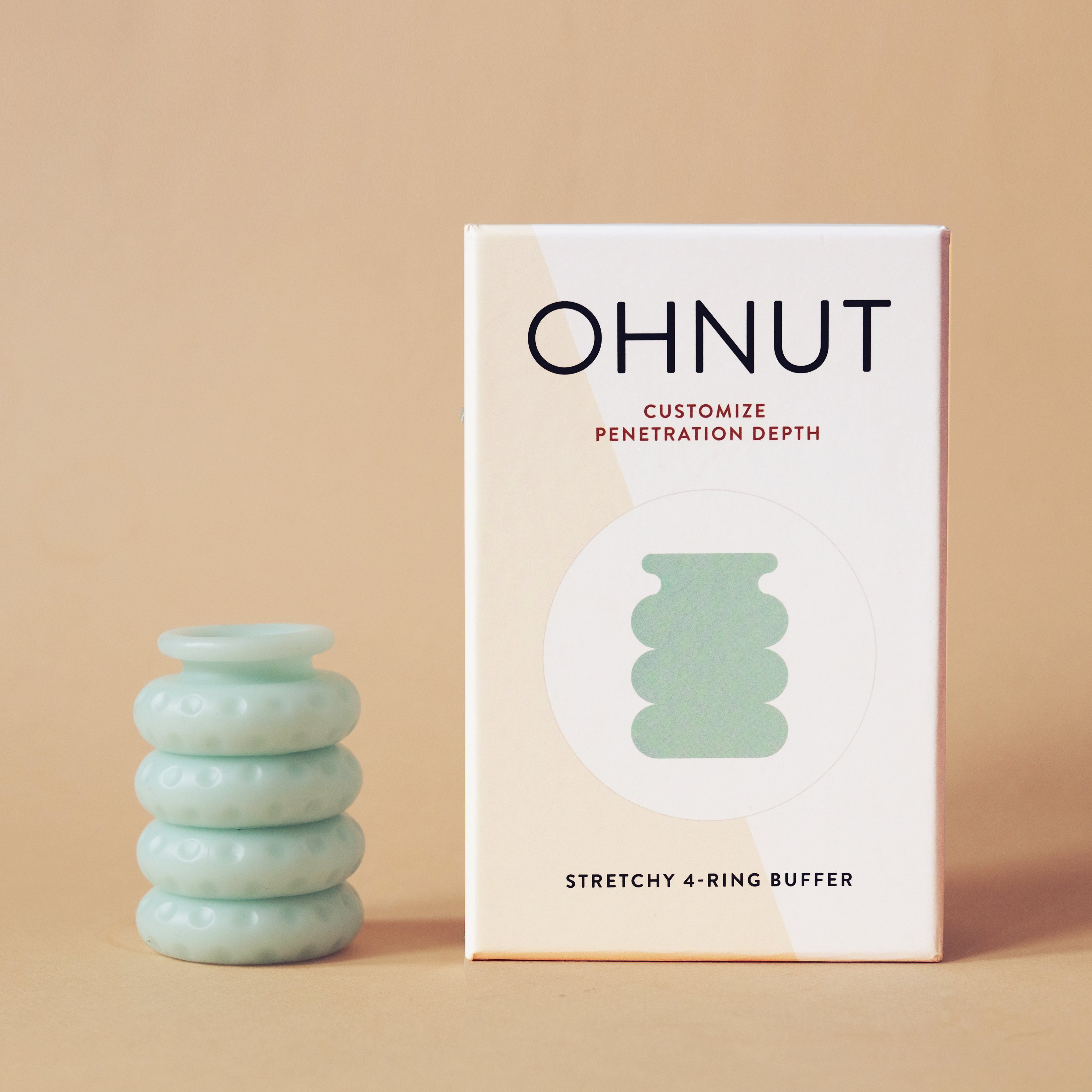 A set of four light green, stackable Ohnut Buffer Rings sits beside its beige and white box labeled "Ohnut: Penetration Depth Control." The stretchy, body-safe silicone rings are displayed on a neutral background.